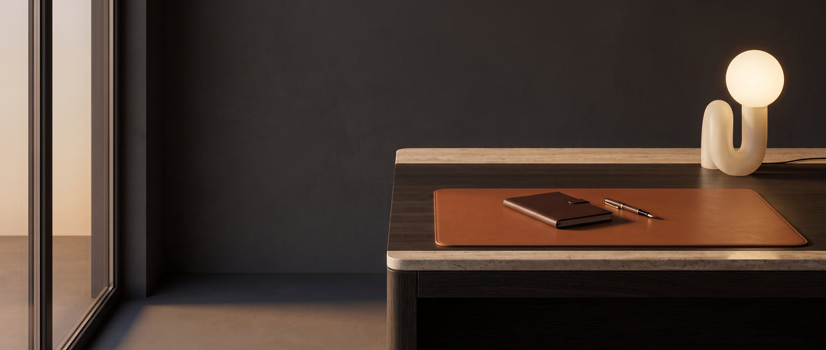 Cognac leather desk mat on a dark oak desk with a glass globe lamp